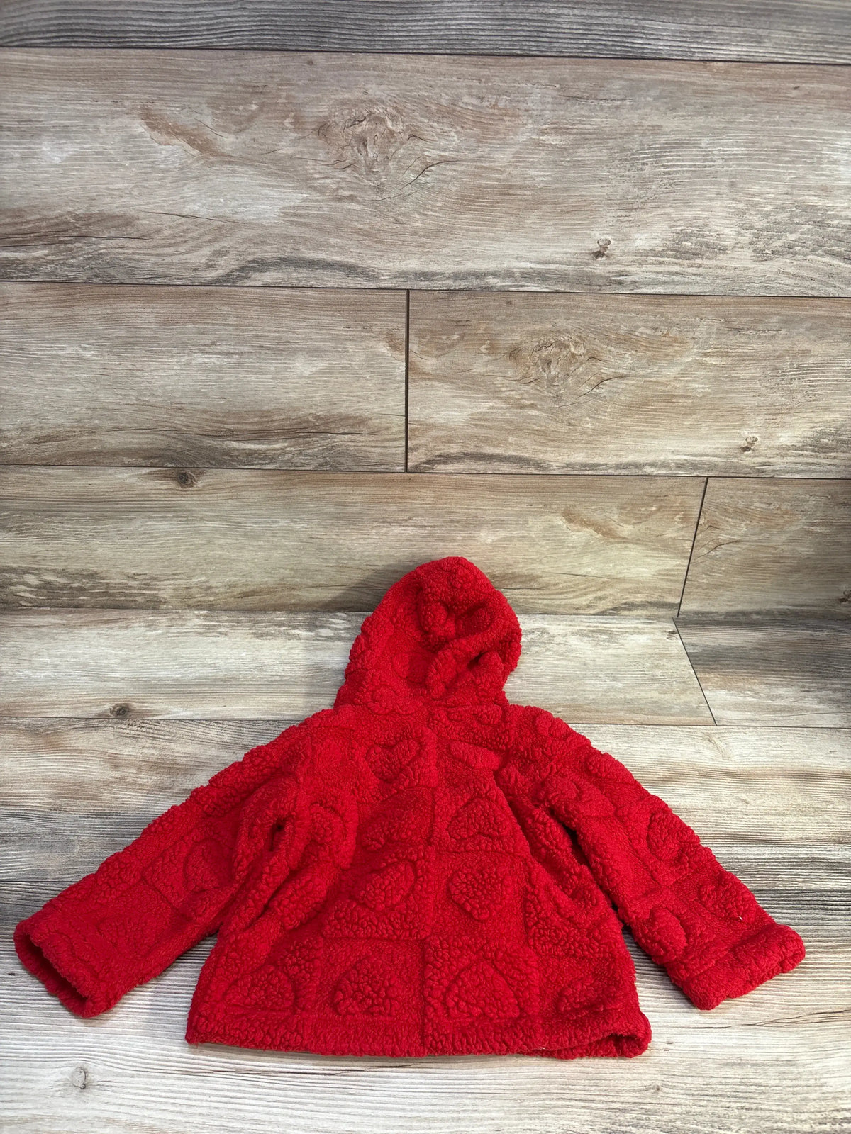 Flat lay of red sherpa hooded jacket size 12 months showing raised heart texture and button up front on wood background