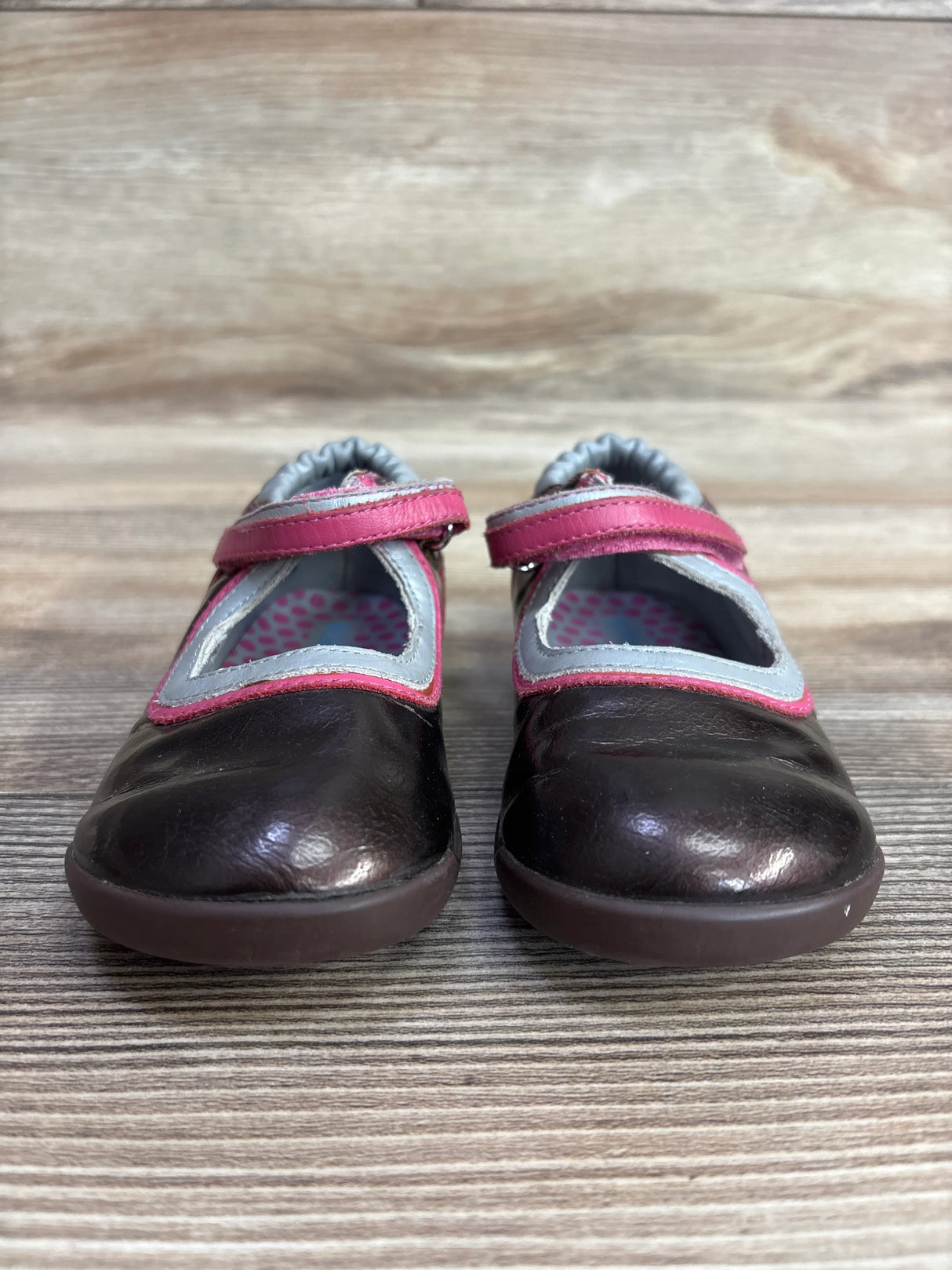 Brown leather toddler Mary Jane shoes with pink straps and gray trim on wood floor