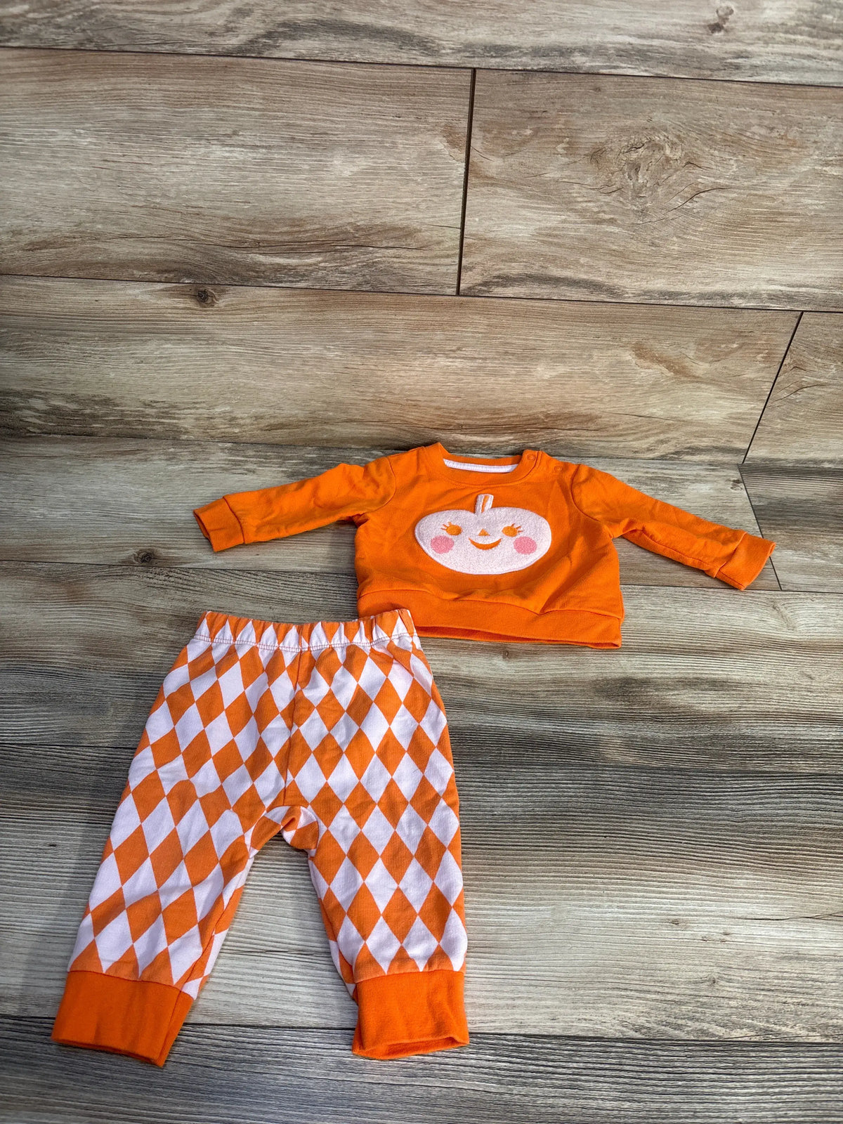 Flat lay of Cat & Jack pumpkin sweatshirt and joggers set with pumpkin face and argyle pattern on wood flooring