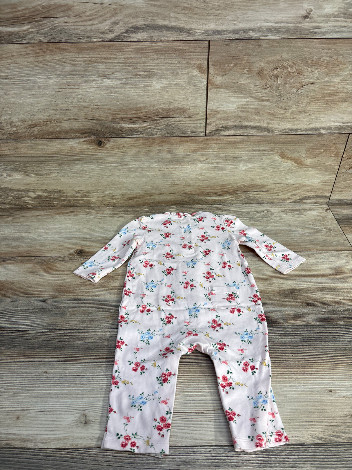 Baby pink floral long-sleeve onesie laid flat on wood floor from children's resale store