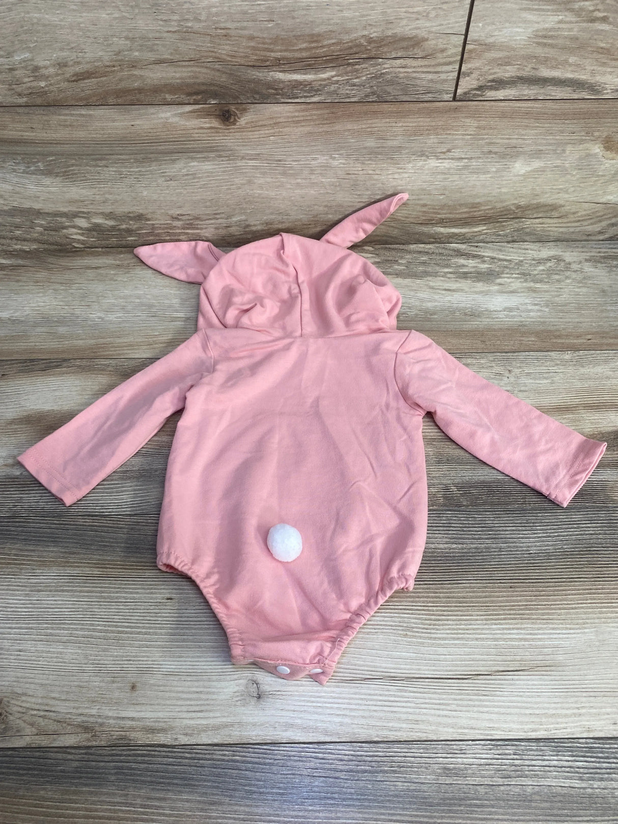 Flat-lay back view of pink bunny romper with hood ears, white pom tail and snap crotch on wood floor