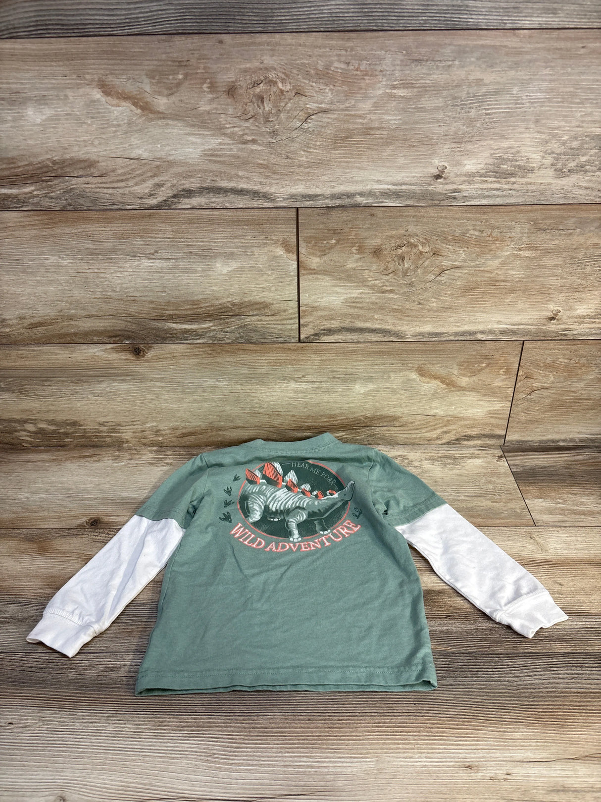 Kids dinosaur long sleeve shirt with 'Wild Adventure' graphic, green and white, on wood floor