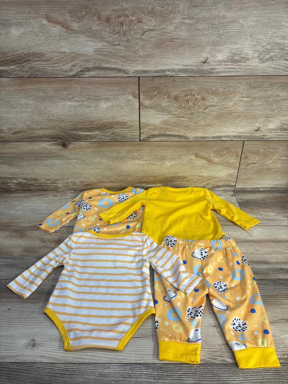 Overhead view of Shein yellow bodysuit and pant set showing three long-sleeve bodysuits and patterned pants on wood flooring
