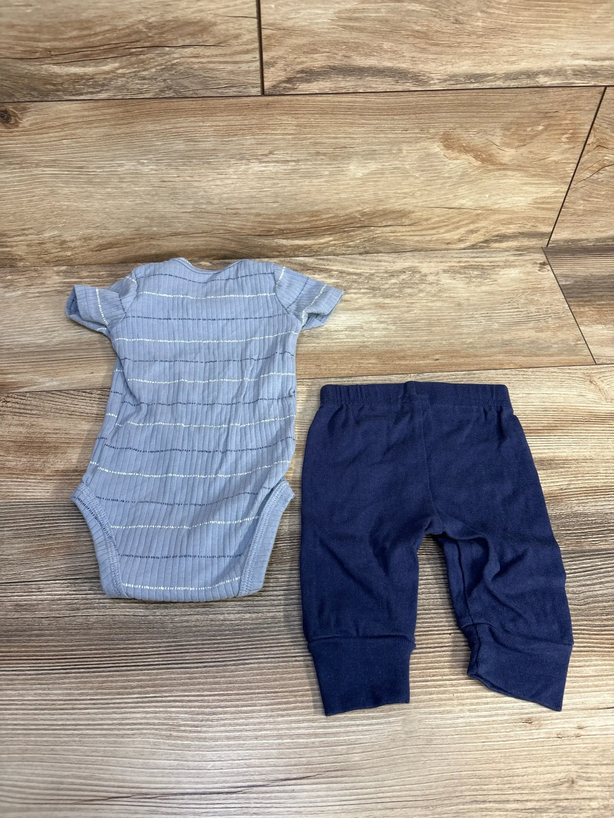 Flat lay of light blue ribbed baby bodysuit and navy pants showing silver stripes and elastic waistband on wood background