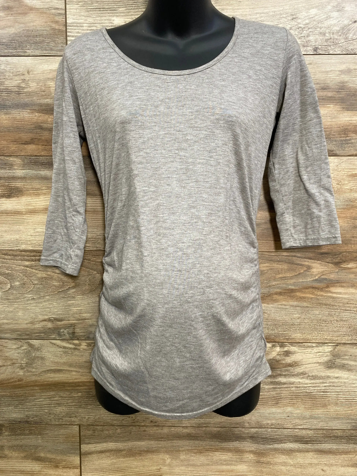 Front view of gray ruched shirt in size small showing three quarter sleeves and gathered sides against wood backdrop