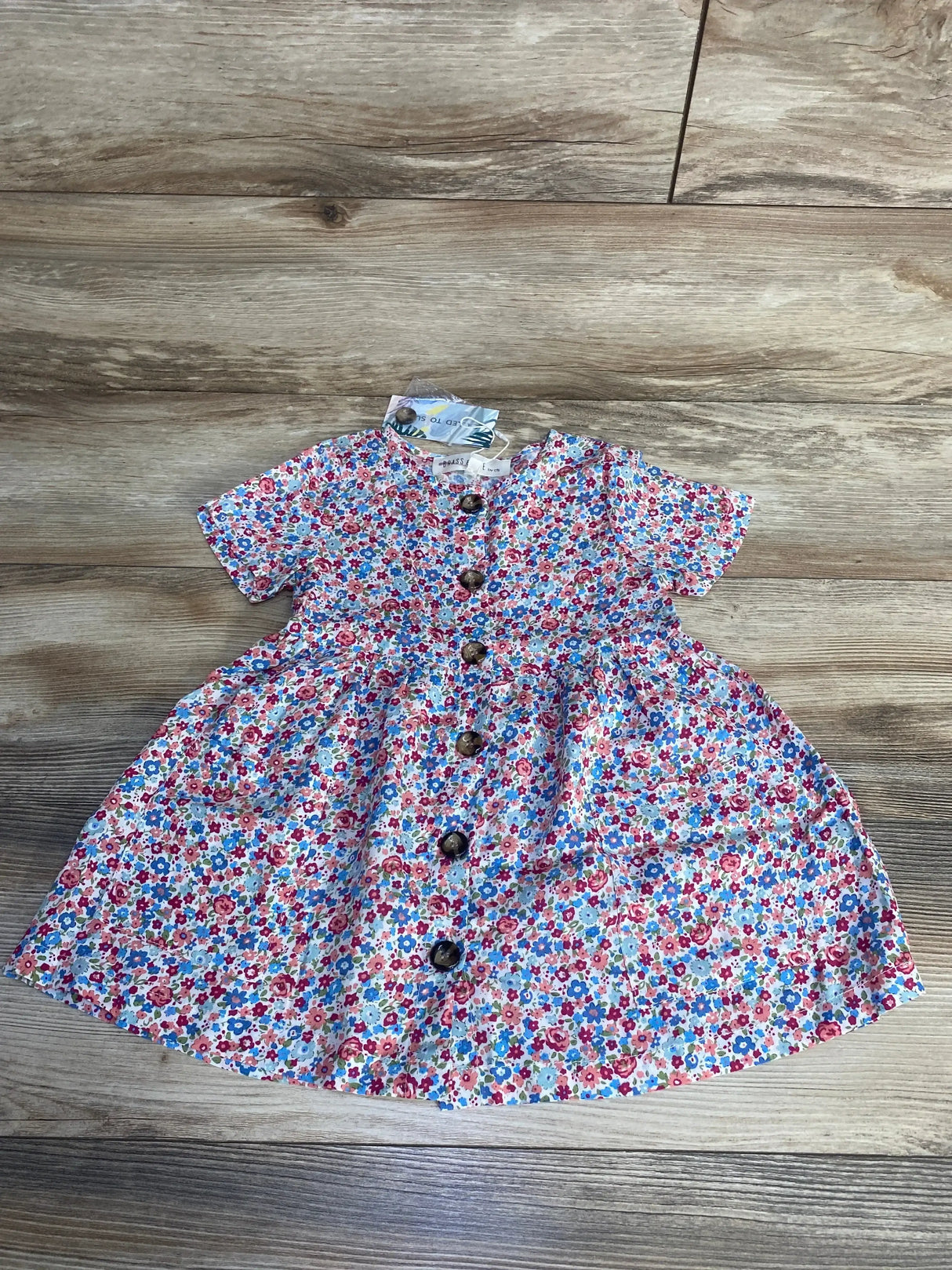 Flat lay of Ophelia toddler dress, size 2T, showing center wooden buttons and small multicolor floral print on wood floor