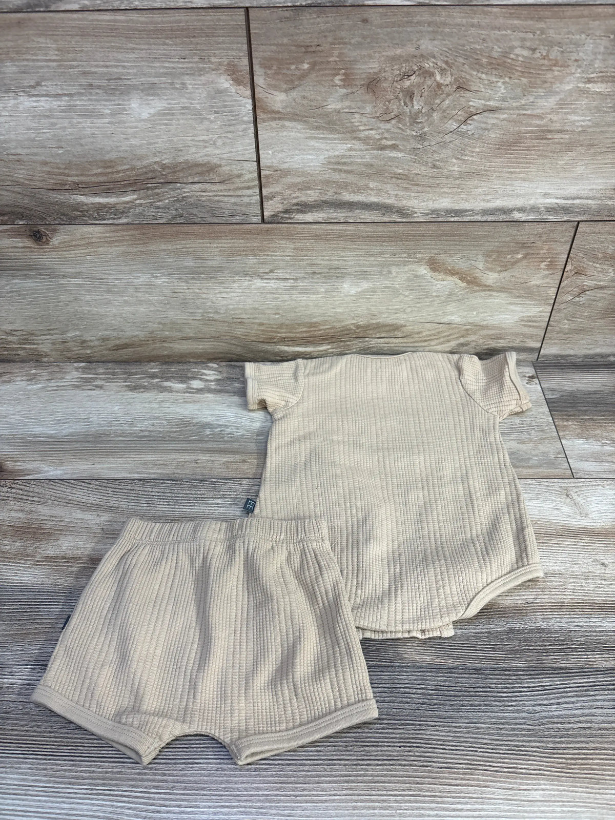 Top-down view of Modern Moments two-piece textured bodysuit and shorts set in tan showcasing ribbed fabric with a wood background