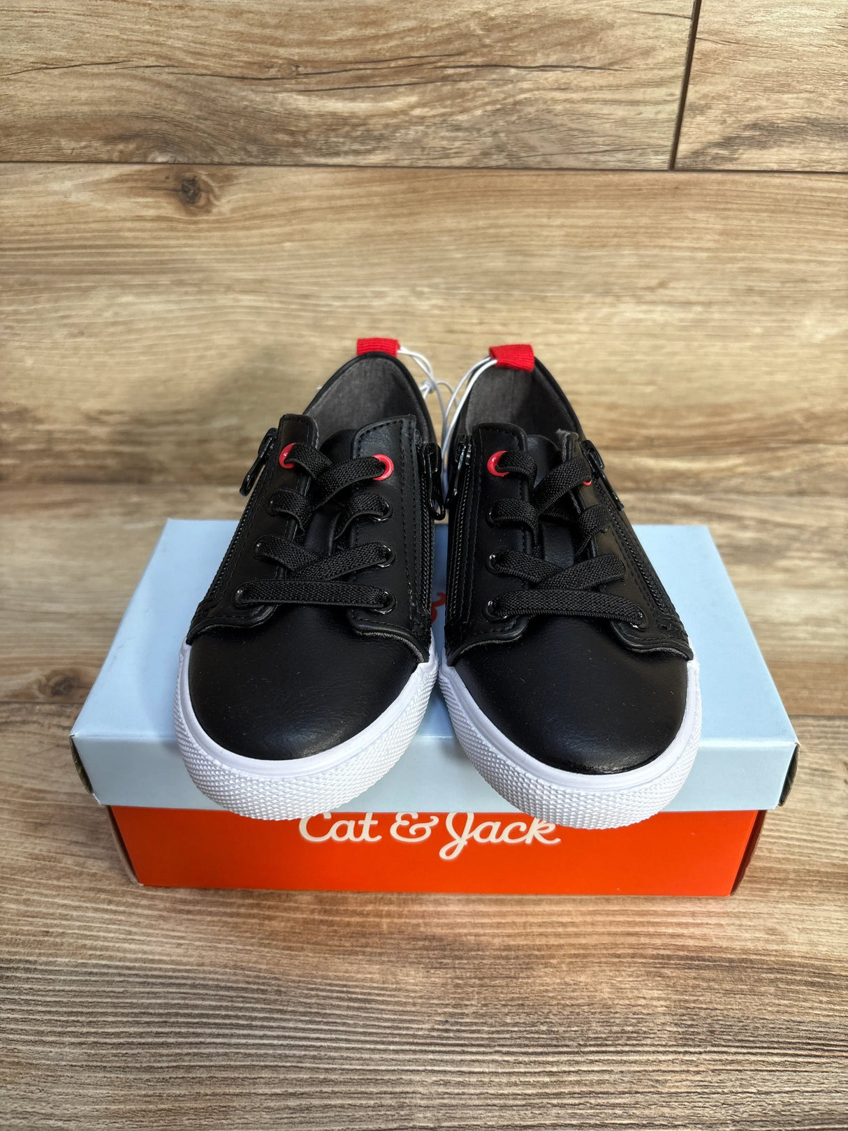 Black Cat & Jack kids sneakers with white soles on a blue and orange shoebox, wood background