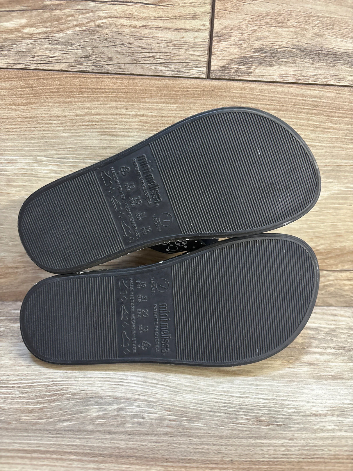 Black Mini Melissa kids shoes soles with ribbed texture on wood floor