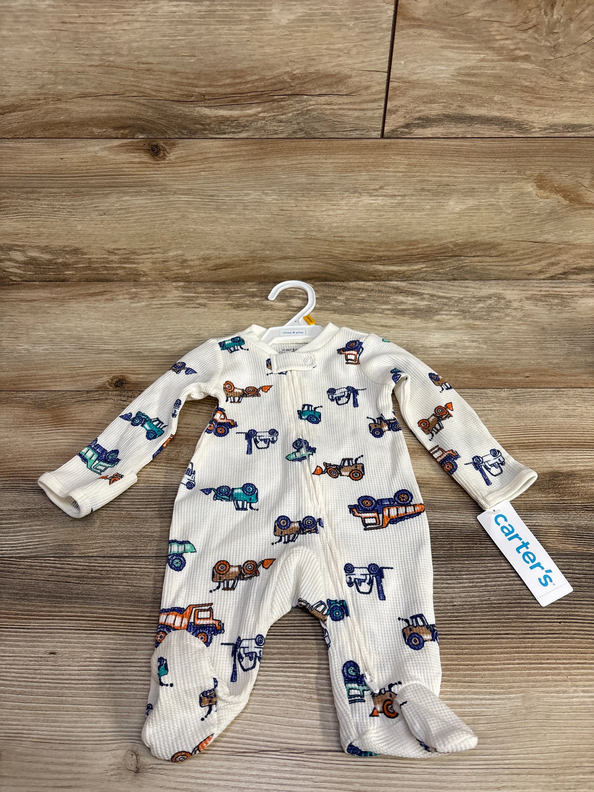Carter's white baby sleeper with colorful construction truck prints on wooden floor