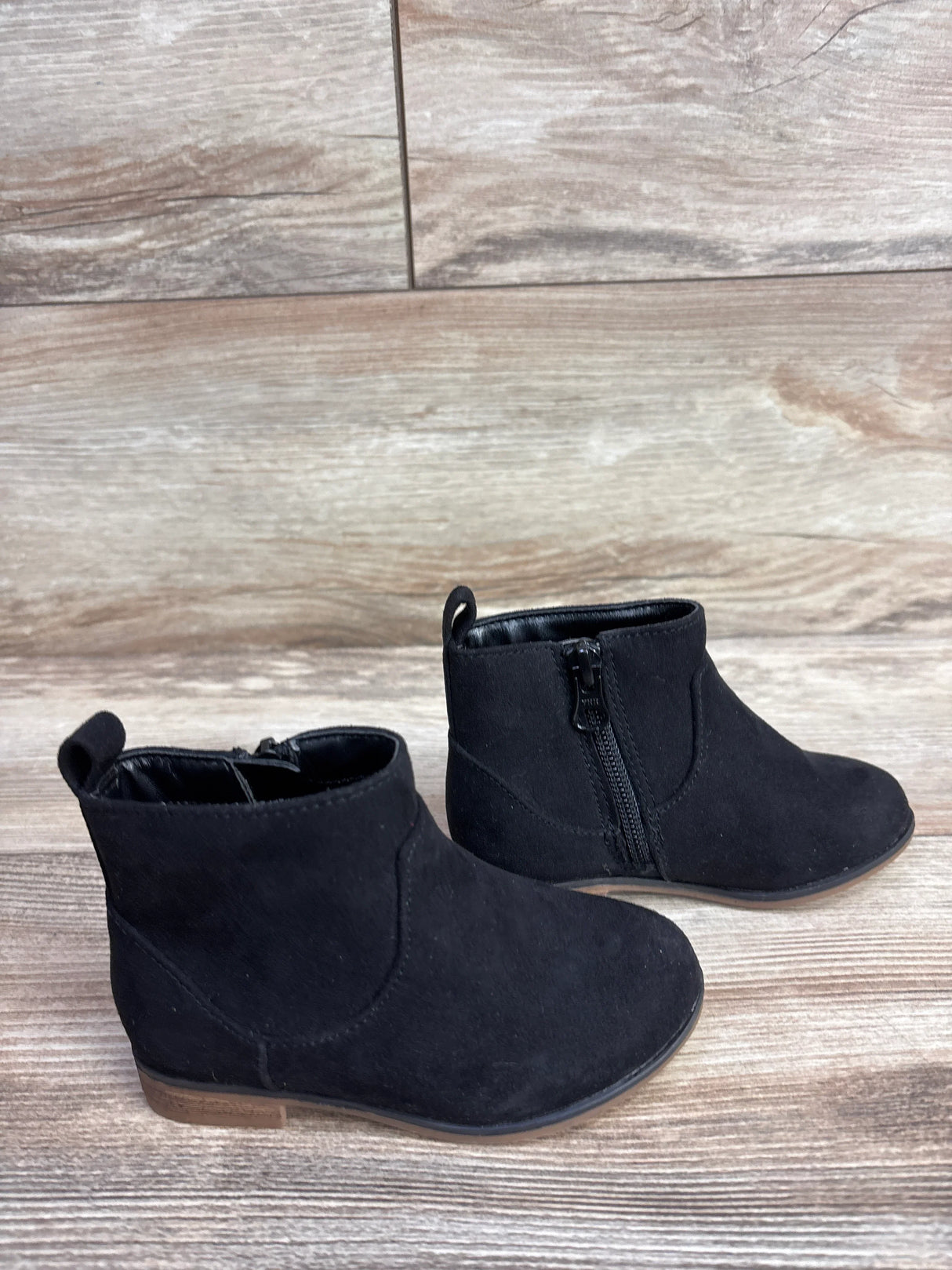 Black suede kids ankle boots with side zippers on wood floor