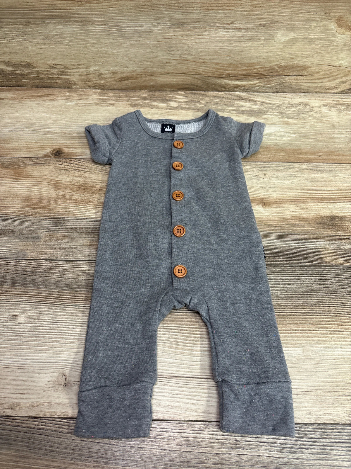 Front view of Littlest Prince Couture gray button-front jumpsuit with five wooden buttons on a wood plank background