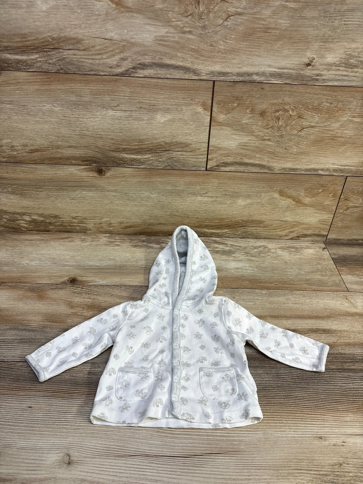 Front flat-lay of Ralph Lauren baby hooded button-up jacket, white with gray animal print and two patch pockets on wood background