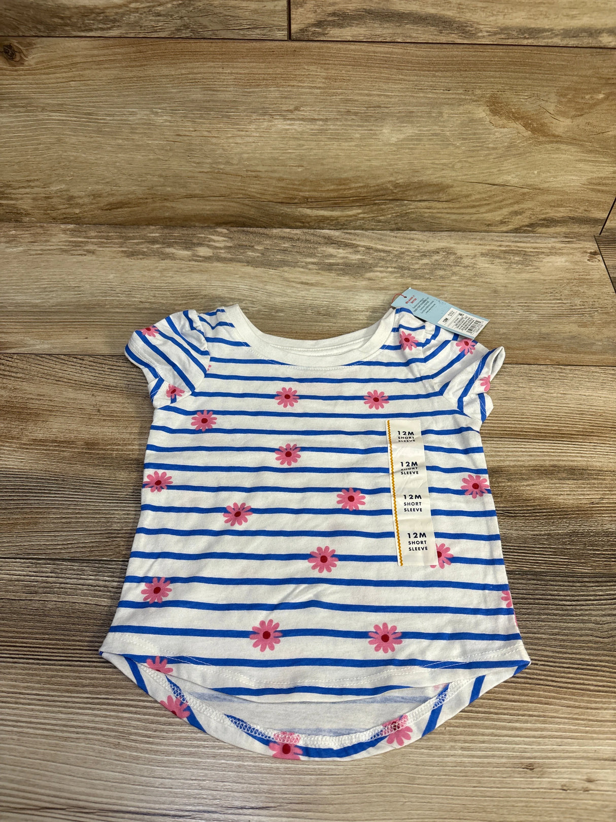 Top view of Cat & Jack 12M short-sleeve shirt with blue stripes and pink daisies on wood background