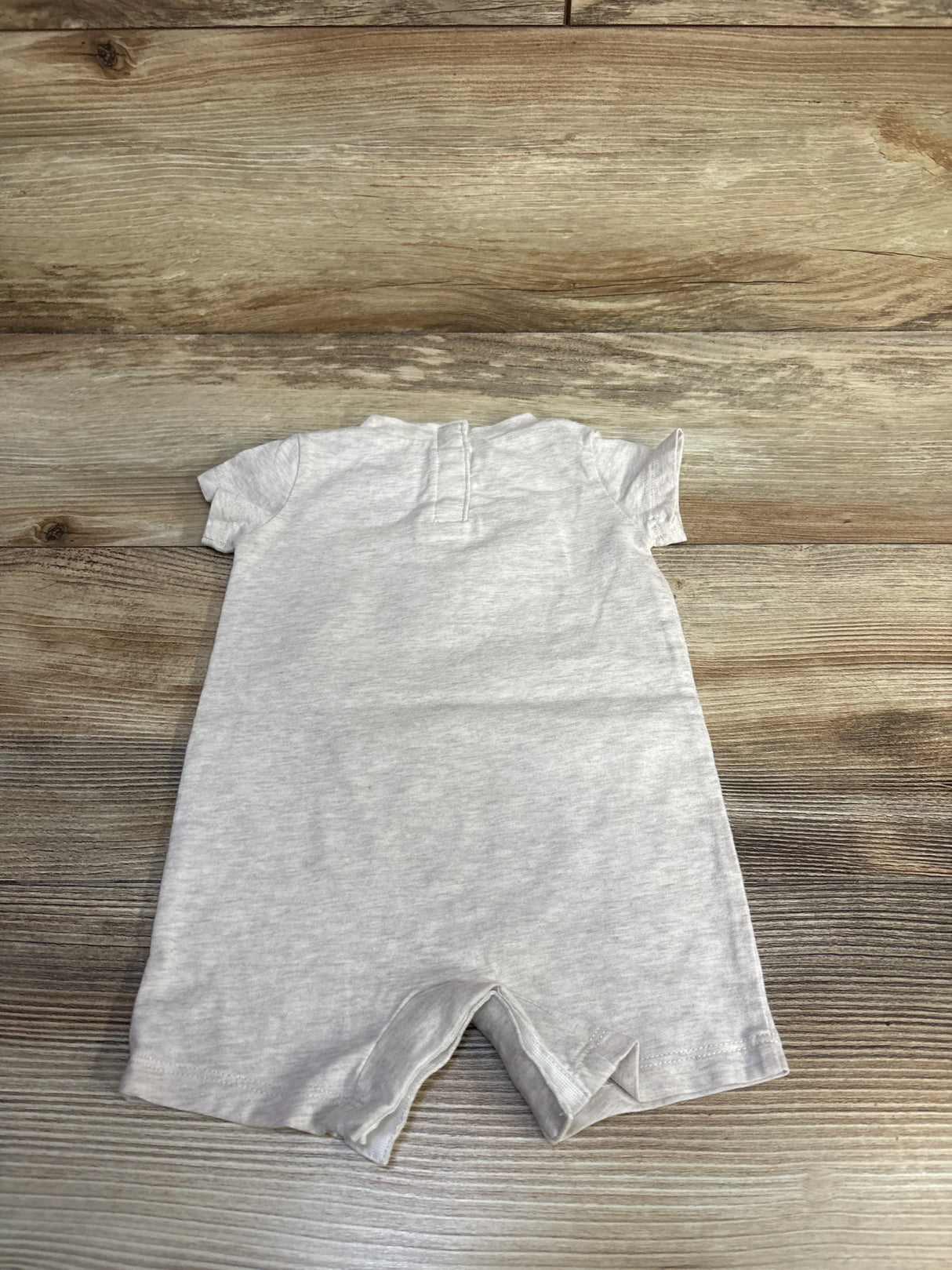Flat-lay back view of beige Nike shortie romper size 3M showing short sleeves and short leg openings on wood background