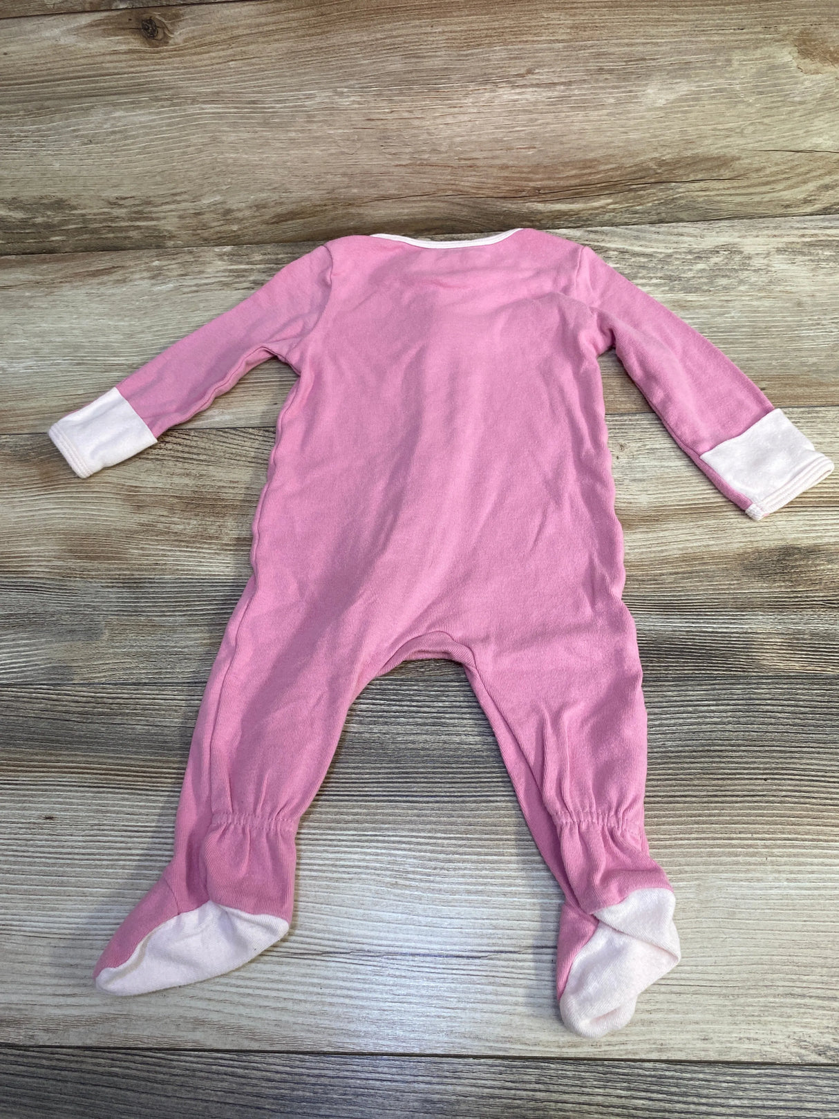 Pink baby footed sleeper with white cuffs and foot soles on wooden floor