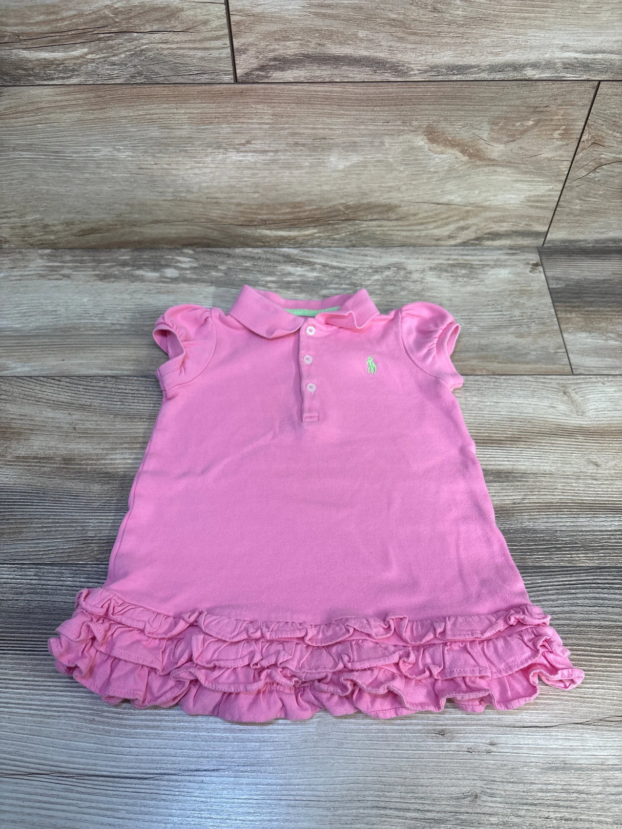 Pink toddler girl polo dress with ruffle hem, cap sleeves, and button collar on wood floor