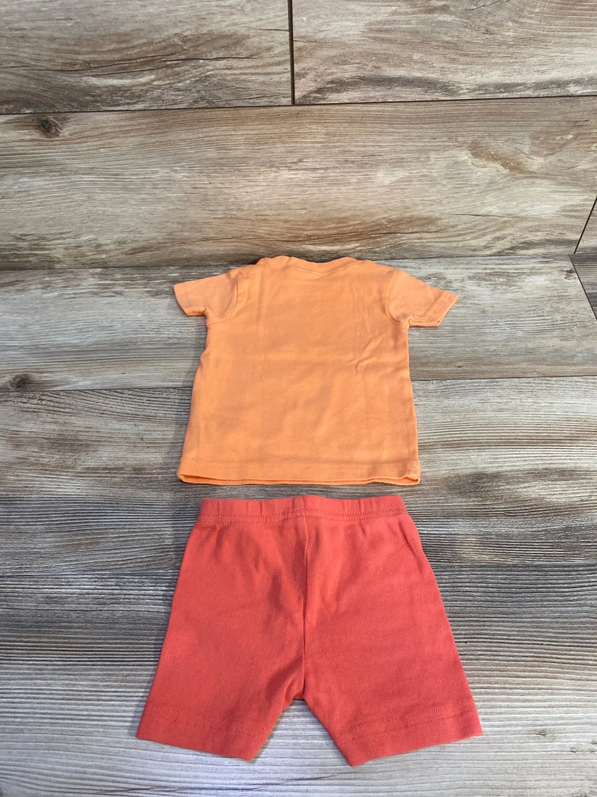 Flat-lay of Carter’s 2-piece pajama set, size 6M, with orange short-sleeve top and coral shorts on wood background