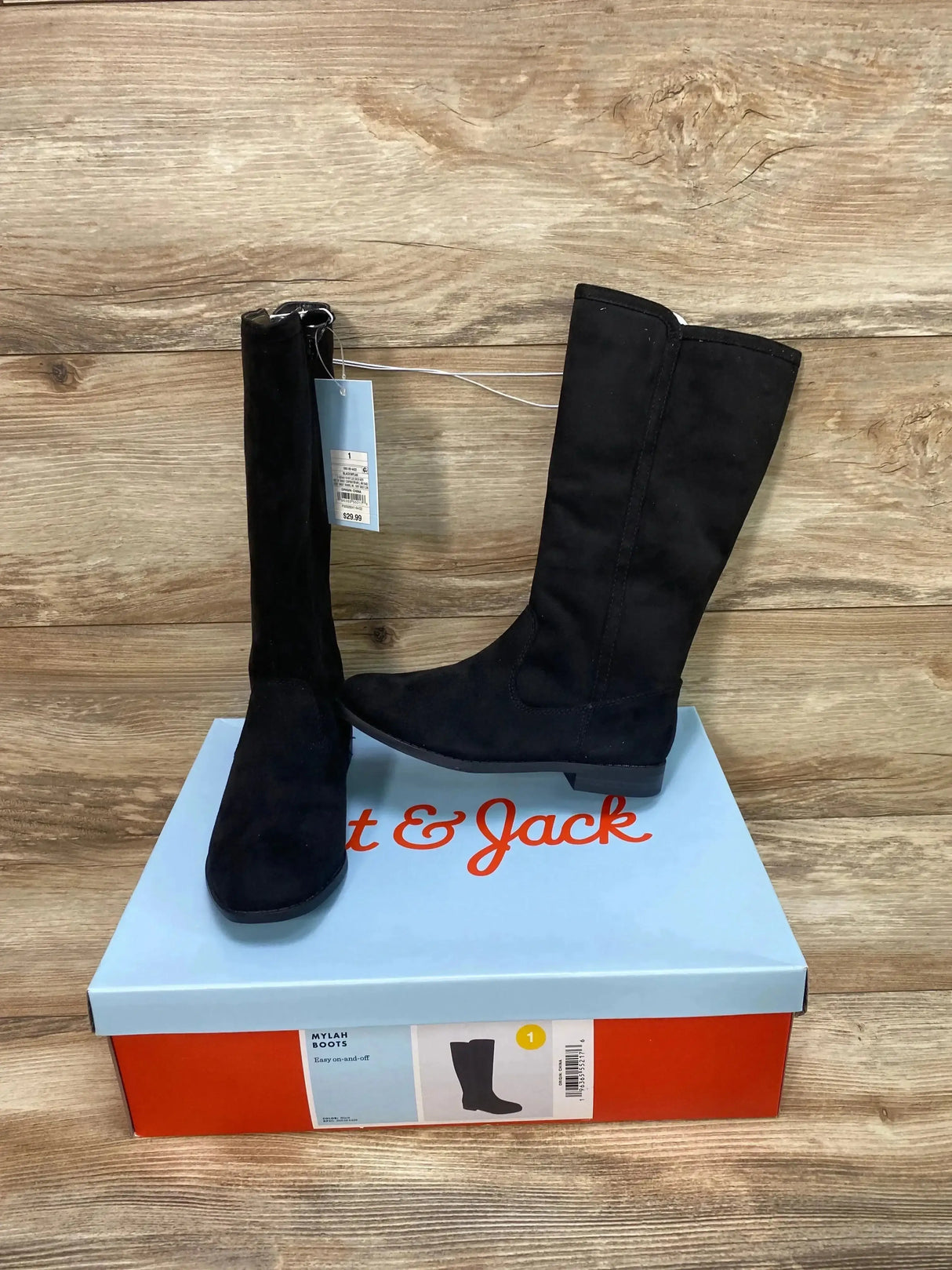 Side view of Cat and Jack Mylah toddler tall black riding boots showing low flat heel on shoebox against wood background