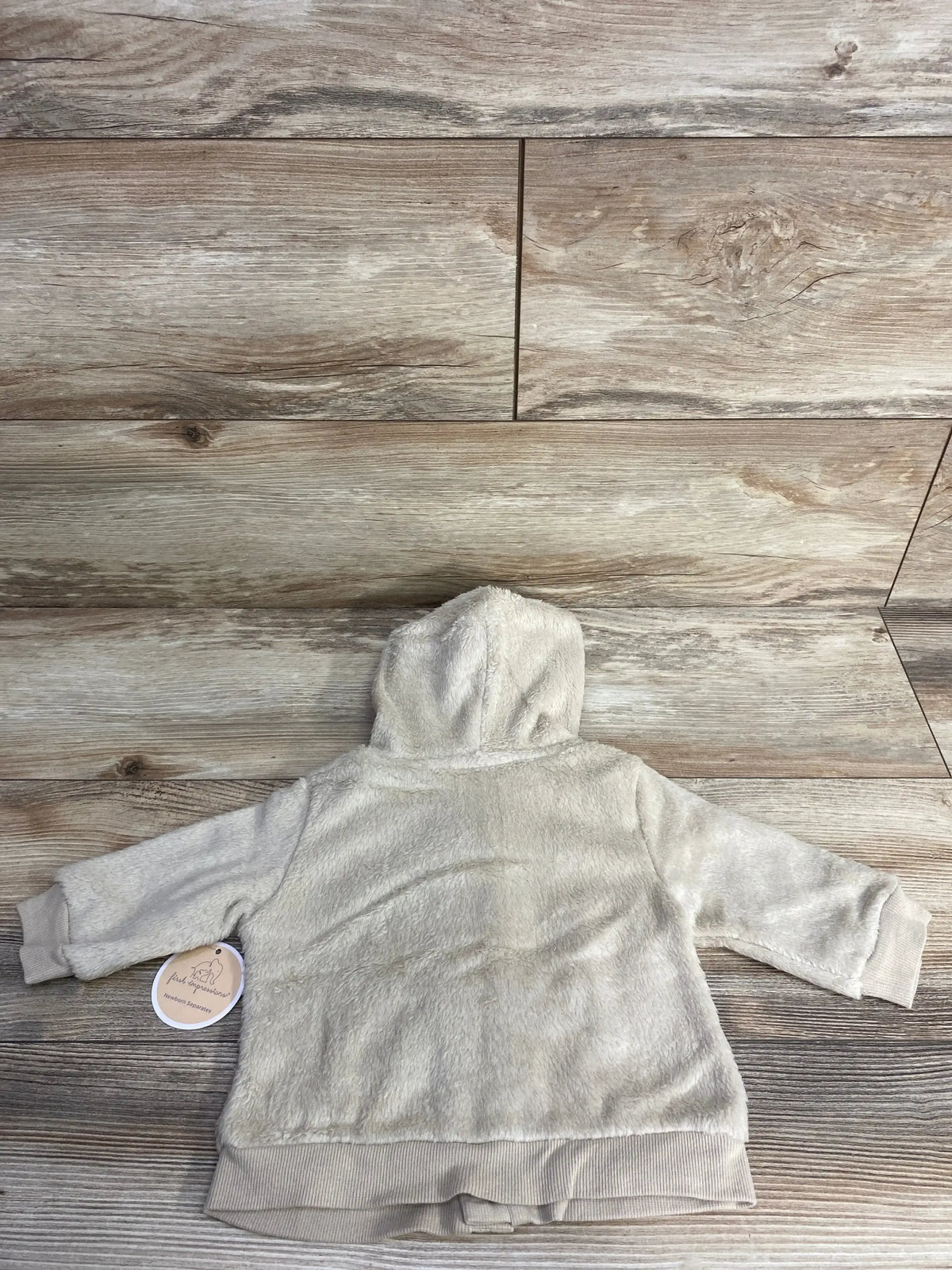 Back view of First Impressions plush button-up hoodie in beige 3-6M showing hood, long sleeves, ribbed hem on wood
