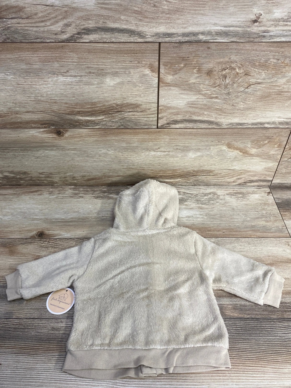 Beige fuzzy baby hoodie with long sleeves, laid flat on wood background