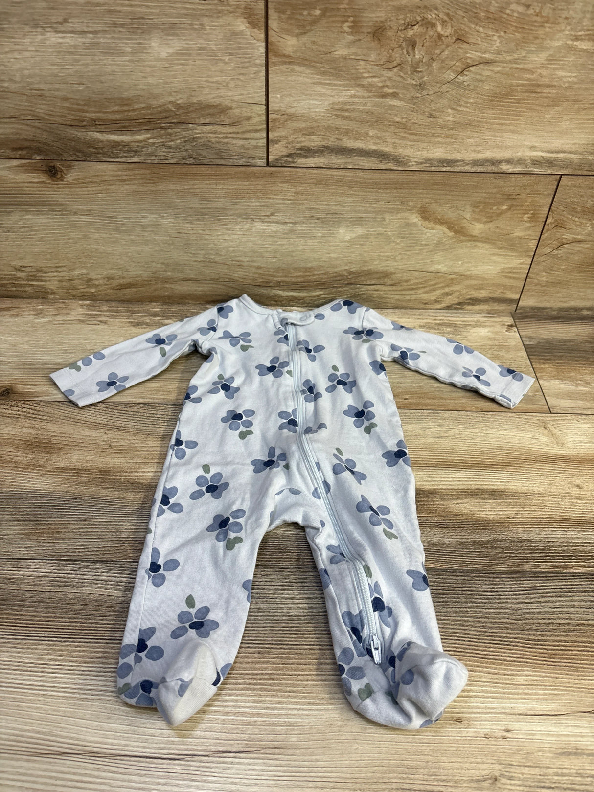 Flat lay of Just One You blue floral footed sleeper showing front zipper, size 6 months on wood floor background