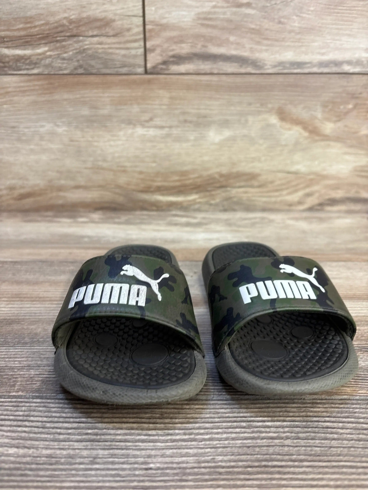 Kid's black camo Puma slide sandals with textured soles on wood background