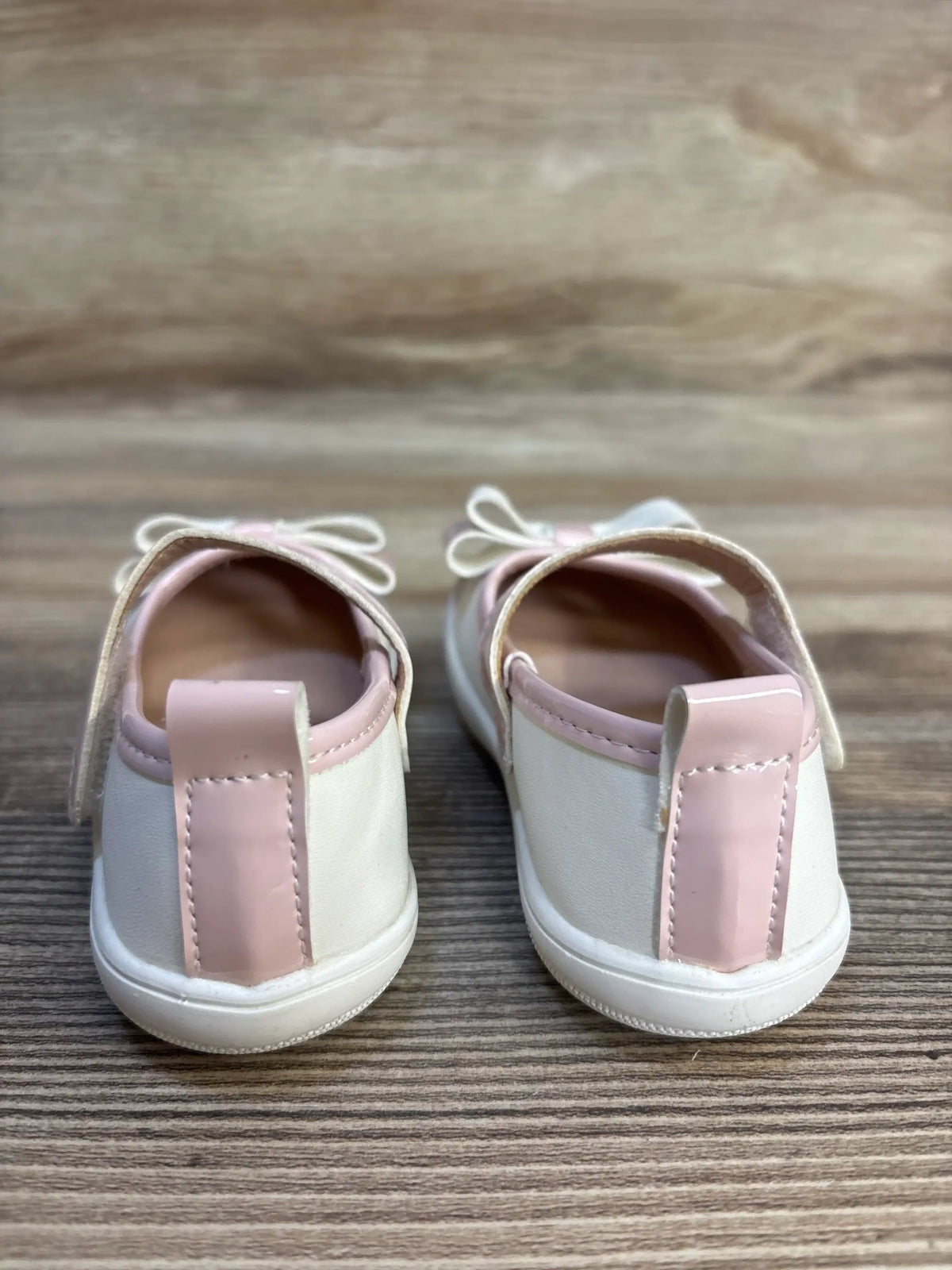 Pair of white and pink baby shoes with bows on wooden background