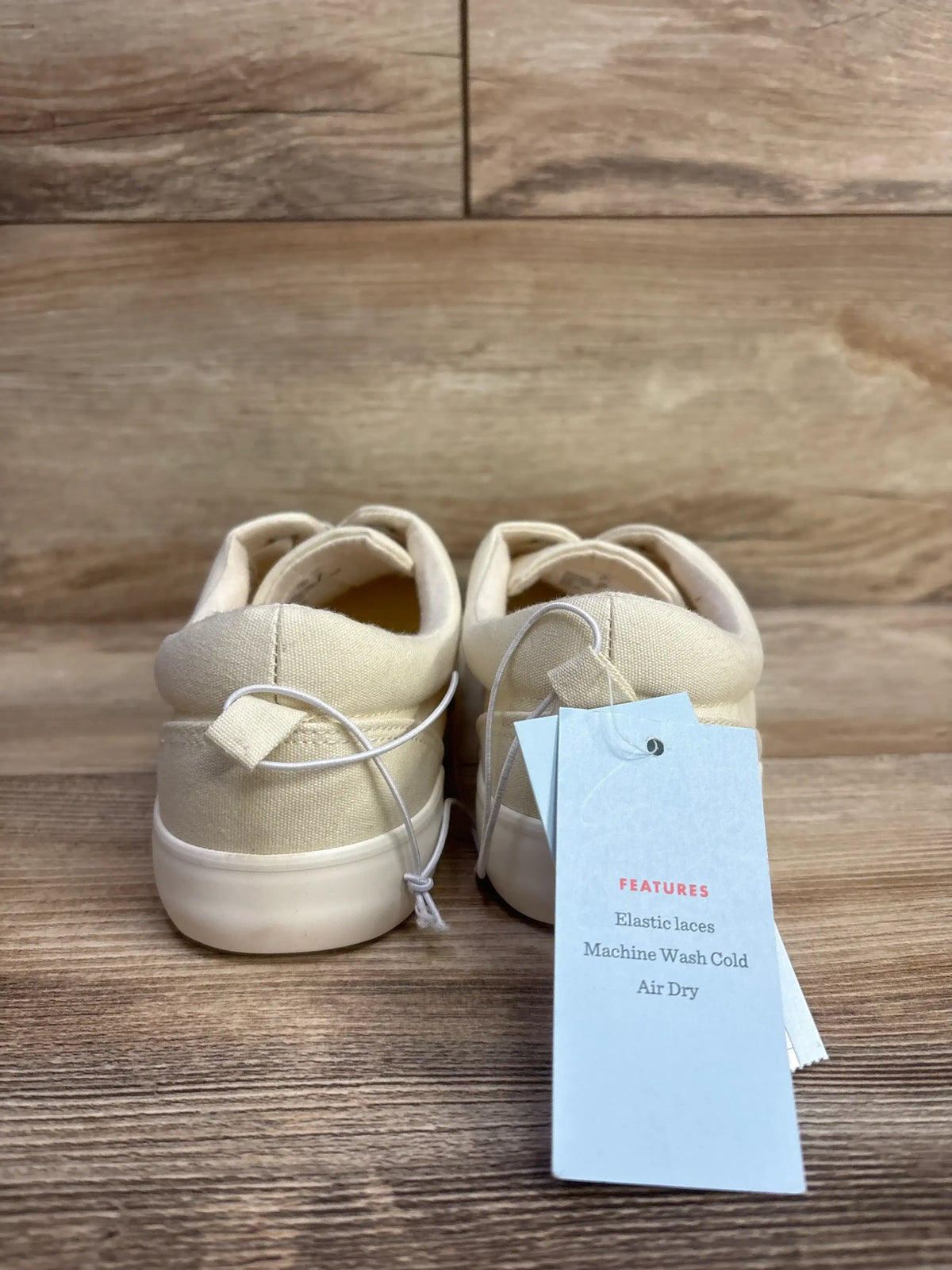 Back view of beige toddler shoes with elastic laces and care tag on wood background