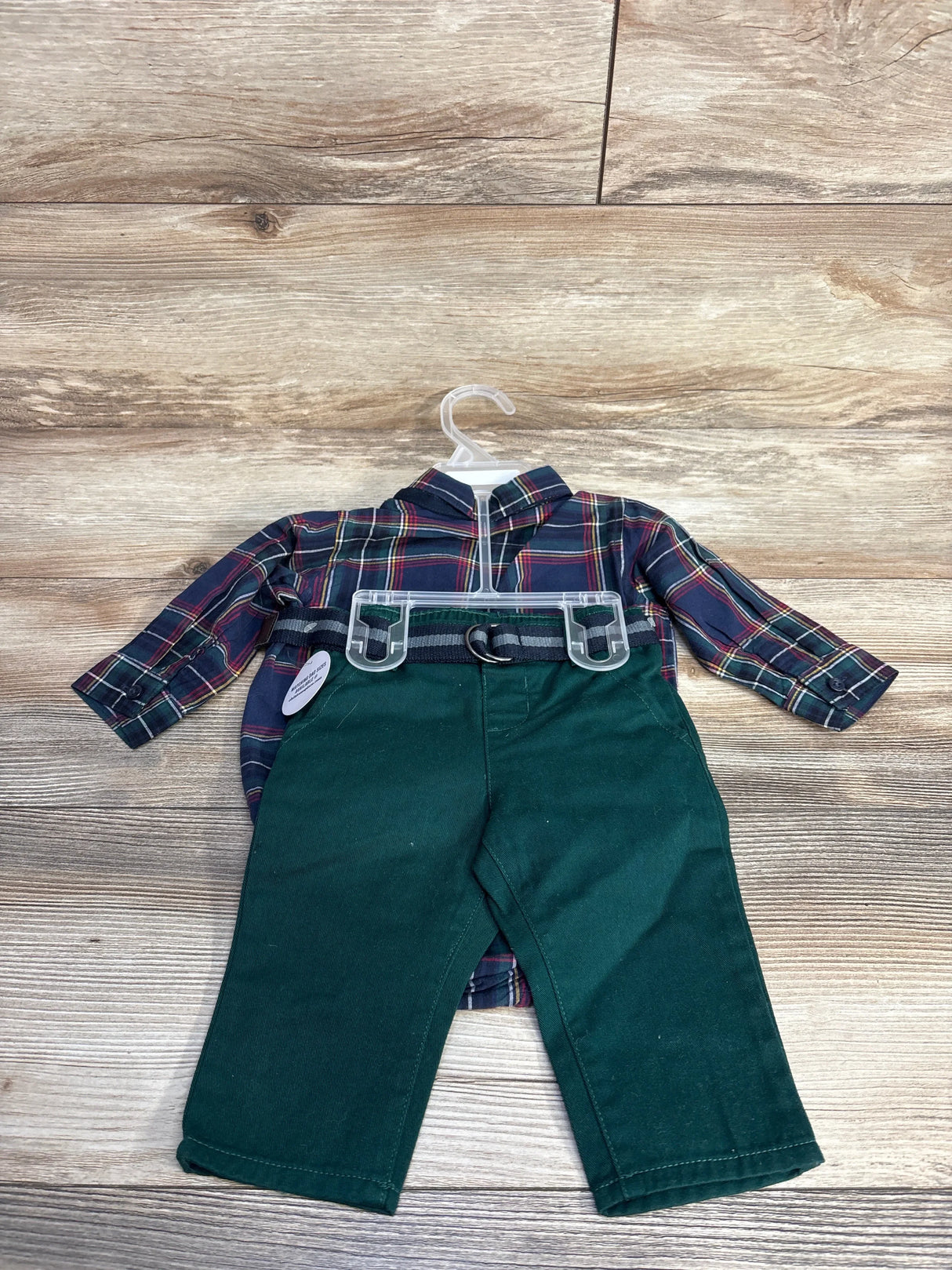 Plaid doll shirt and green pants outfit on hanger, wood background