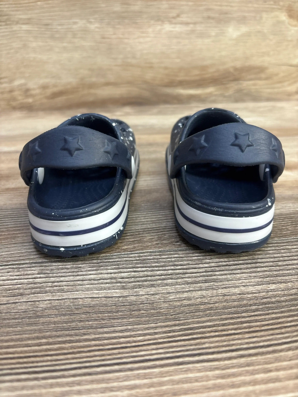 Rear view of Koala Kids star cut-out clogs showcasing star embossed heel strap and white double striped platform on wood background