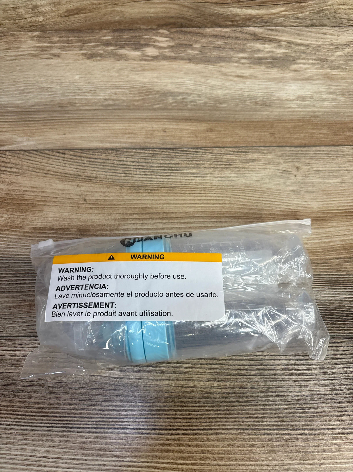 Packaged clear baby feeding bottle with blue cap and warning label on wooden surface