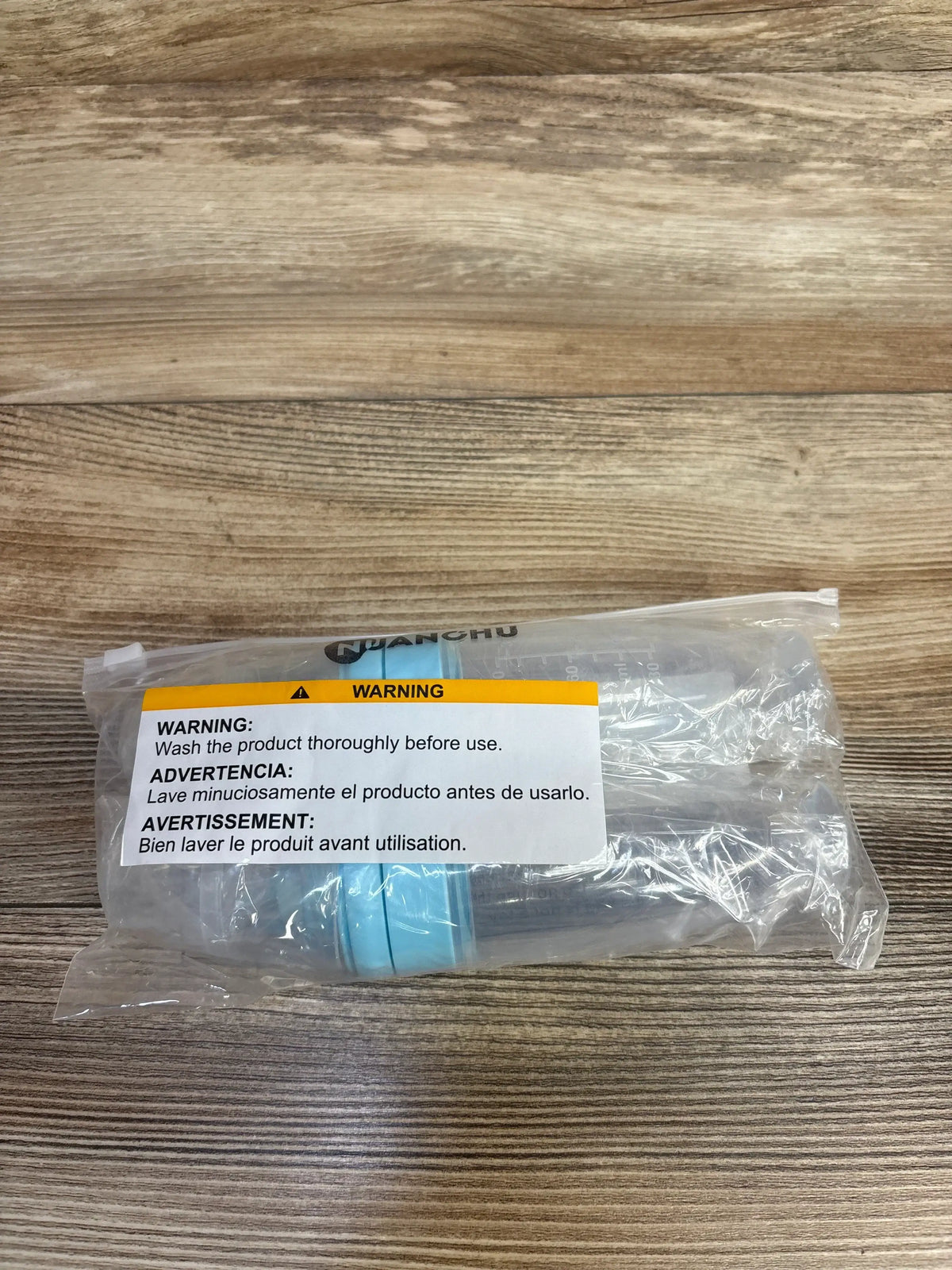 Top view of NEW Nuanchu Silicone Baby Spoons Blue 2pk in sealed plastic packaging with warning label on wood plank background