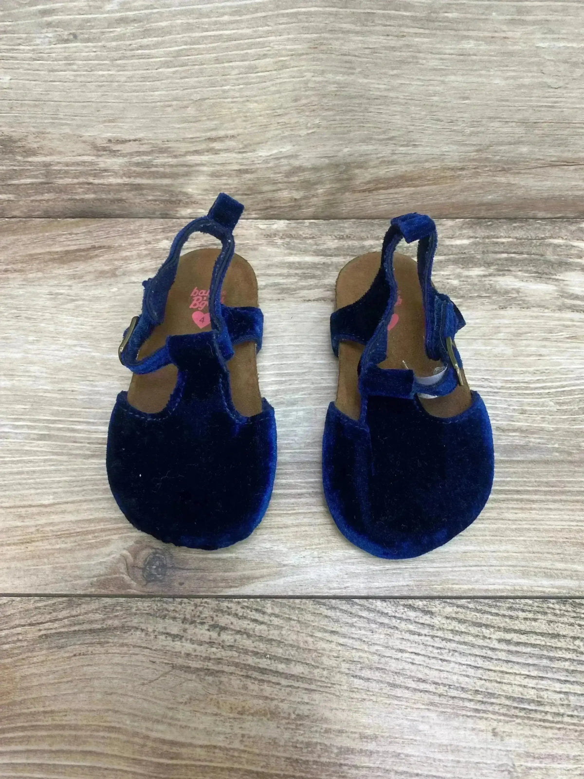 Top view of navy velvet baby sandals showcasing cork footbeds and adjustable ankle straps on light wood background