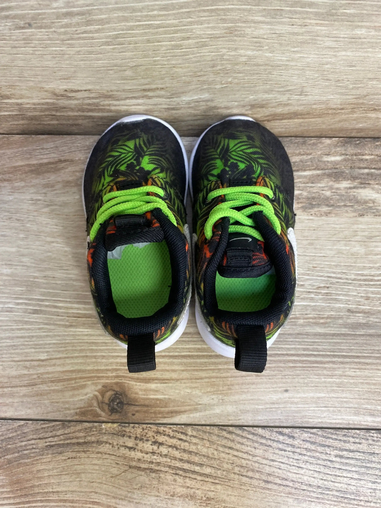 Top view of toddler Nike Roshe Run Print sneakers size 5C showcasing green tropical print and neon green laces on wooden floor