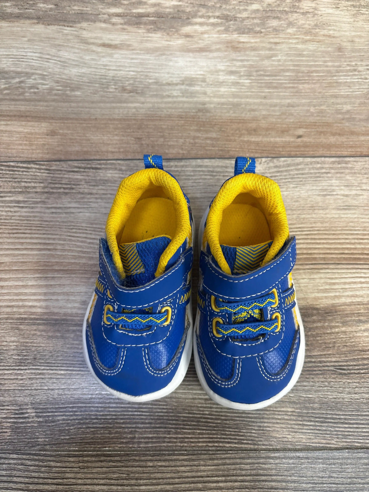 Front view of Wonder Nation blue sneakers, size 3C, showcasing yellow lining and white soles on a wood-grain background