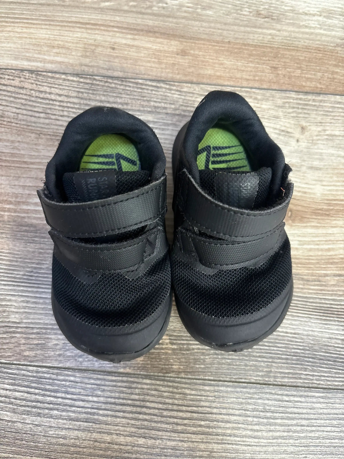 Top-down view of Nike Star Runner 2 TDV toddler sneakers size 4C showing dual Velcro straps, black mesh upper and green insoles on wood floor