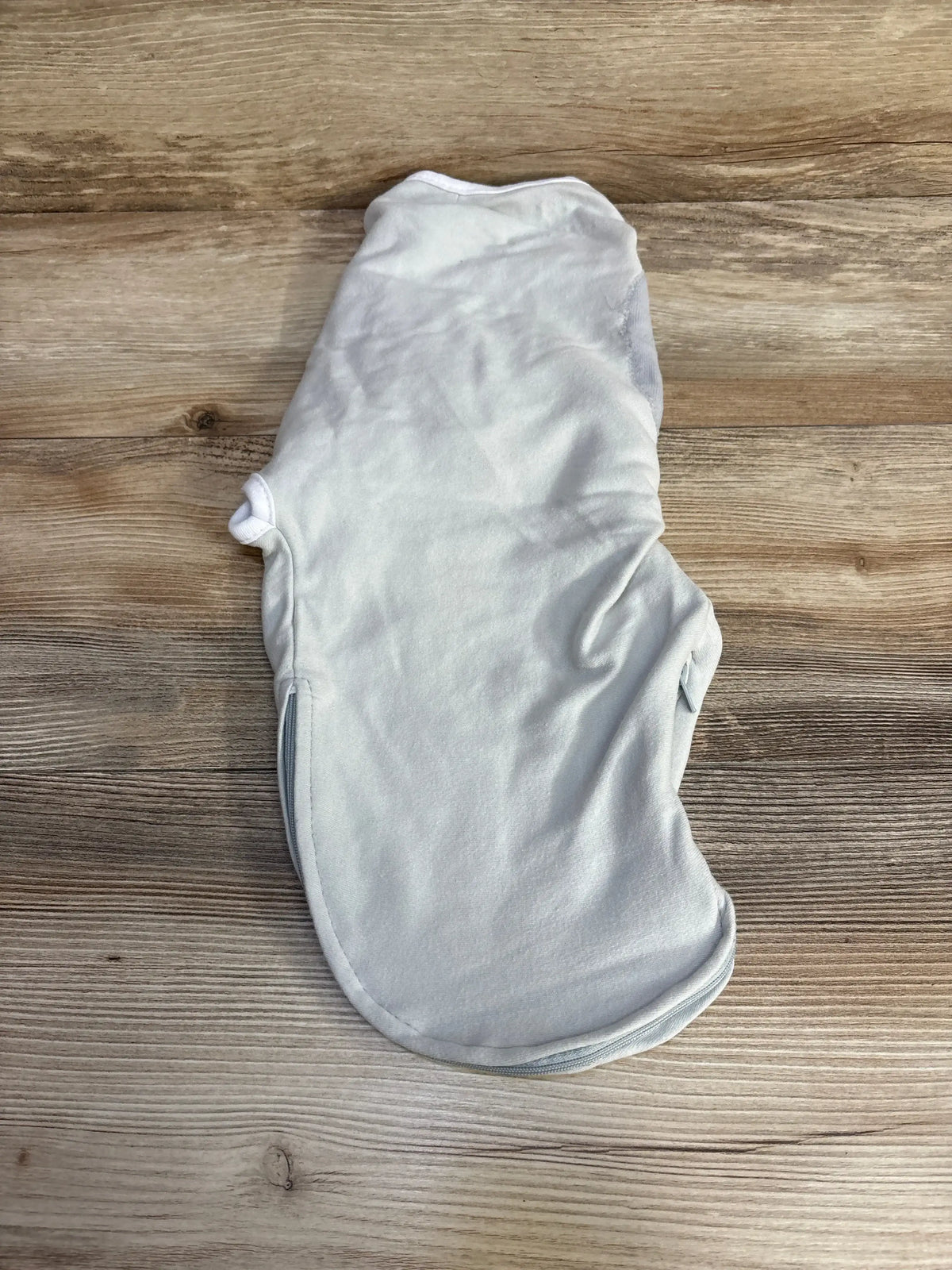 Top-down view of SwaddleMe swaddle wrap in light grey, showing zip closure and winged swaddle shape flat on wood background