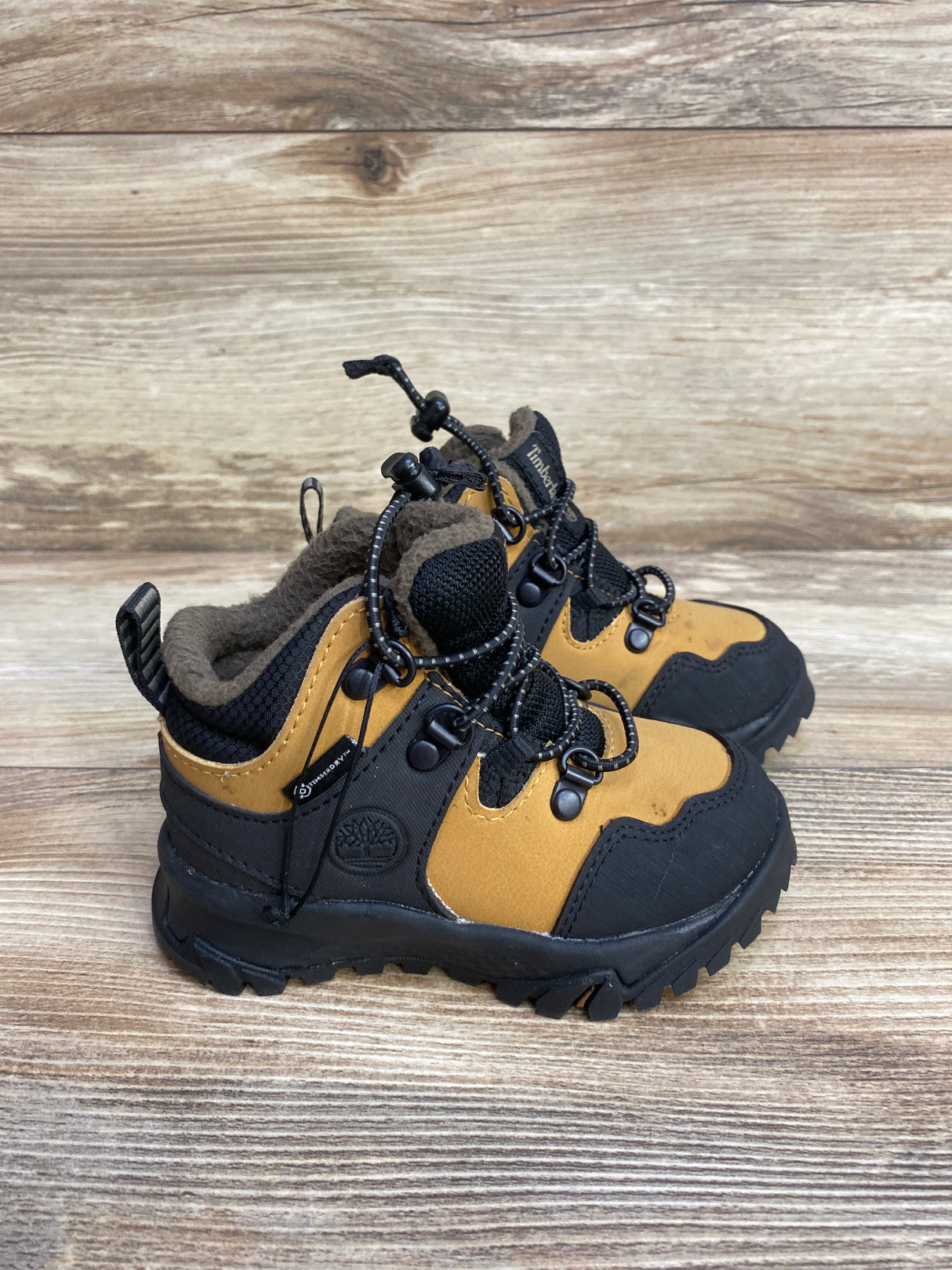 Kids' tan and black Timberland waterproof hiking boots with fleece lining on wood surface