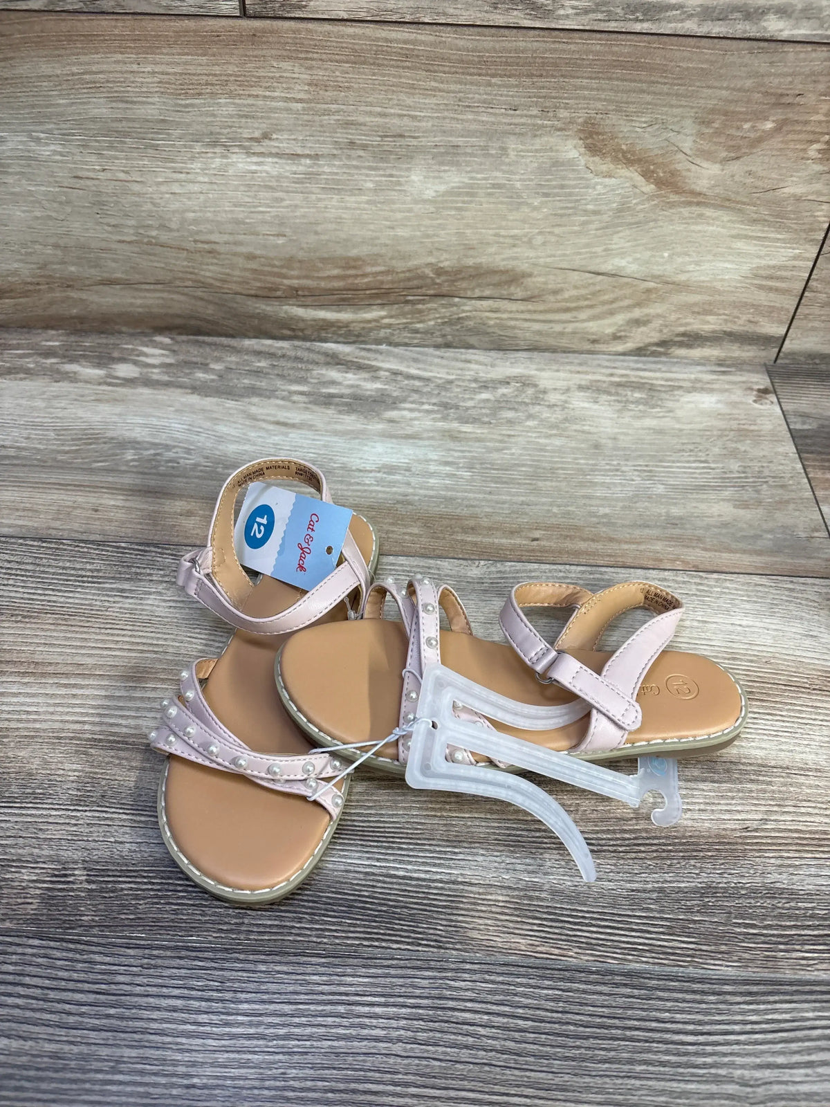 Top view of blush pink Cat and Jack toddler sandals with pearl straps and ankle velcro, on wood plank background
