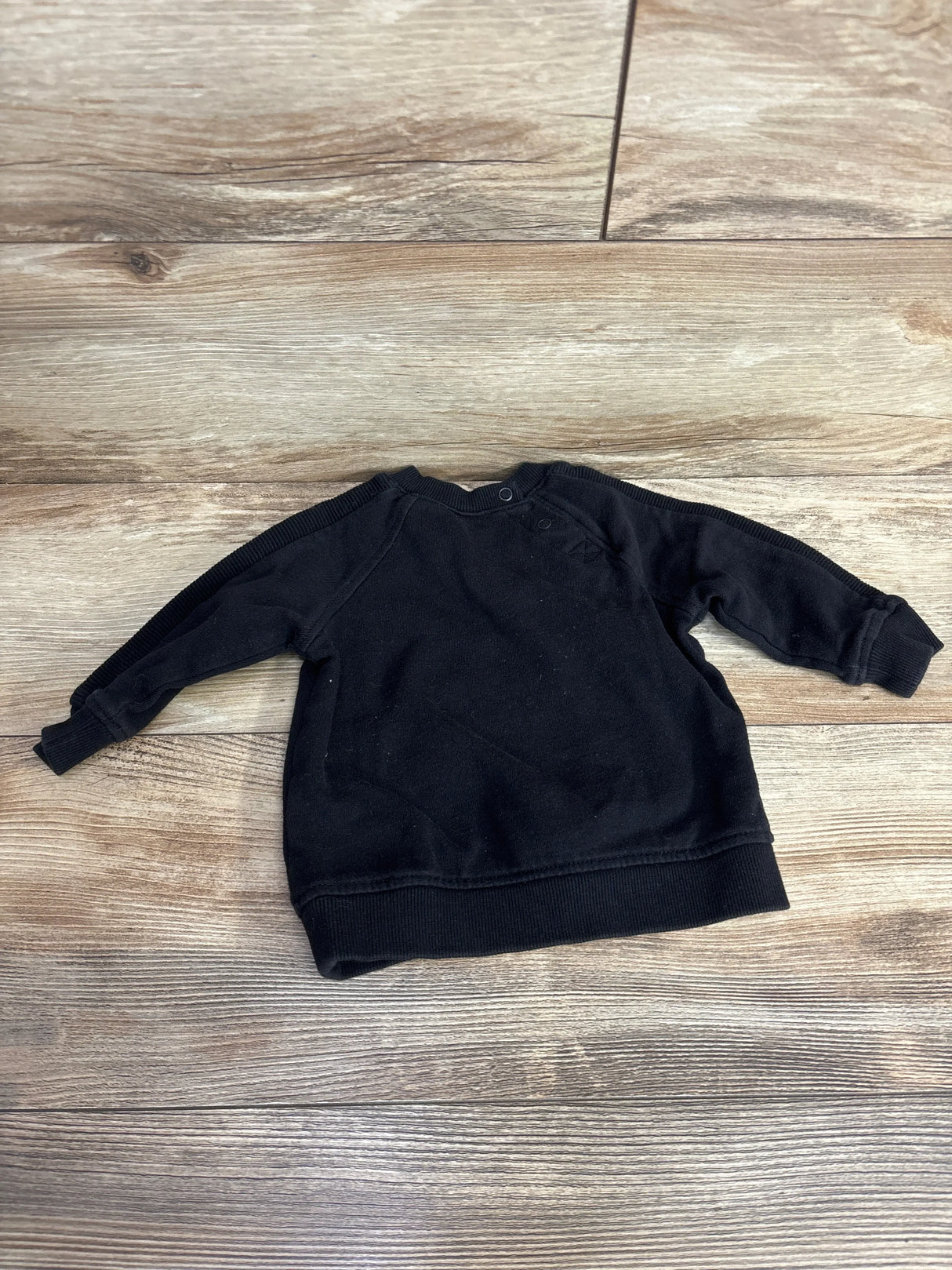 Black long sleeve baby pullover sweatshirt on wood background