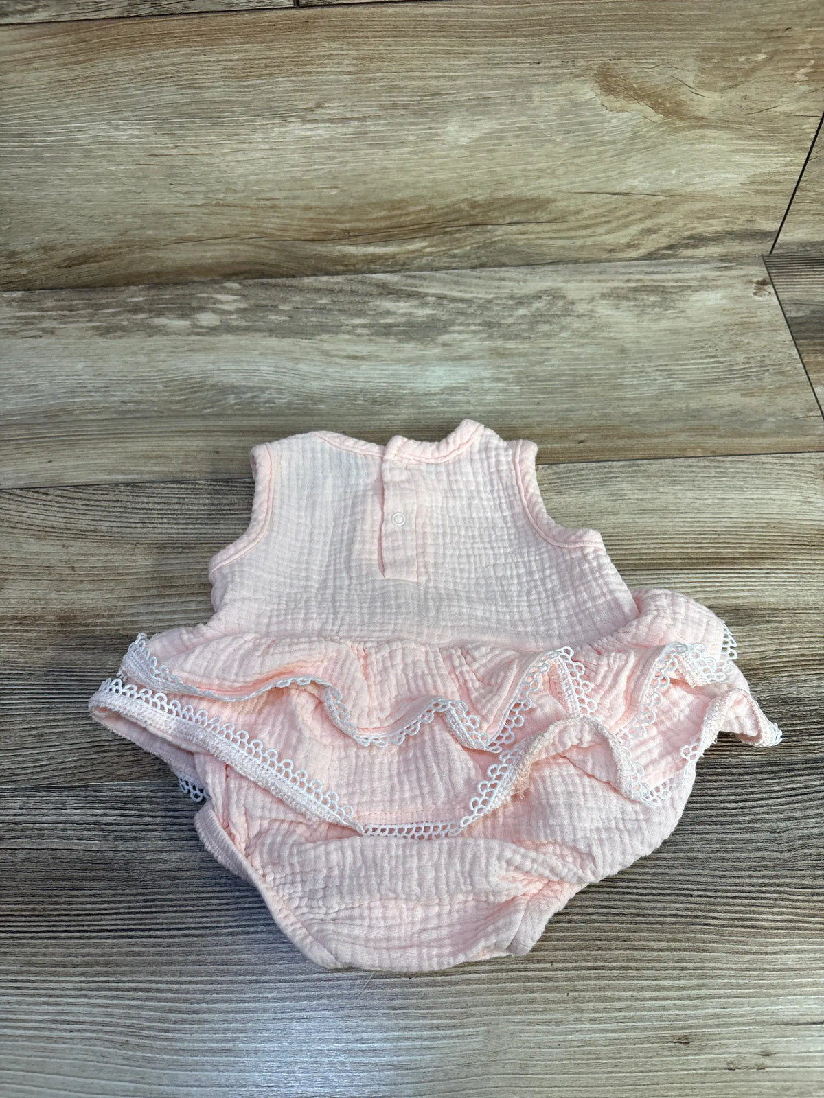 Front view of soft pink RZ by Rachel Zoe gauze lace bodysuit dress with ruffled lace trim and snap closure on wood background