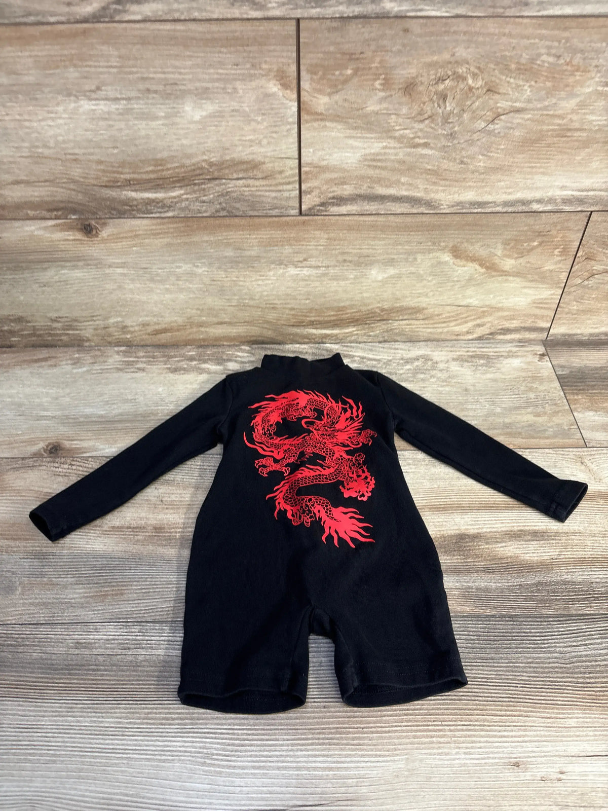 Front view of a black Shein long sleeve dragon shortie romper showcasing its red dragon graphic with a wood-look floor background