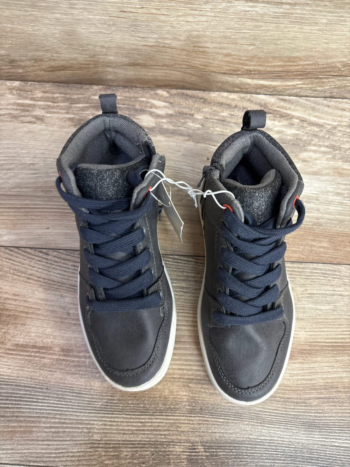 Top-down view of kids' grey high-top sneakers showing navy laces, padded ankle collar, and white soles on wooden floor
