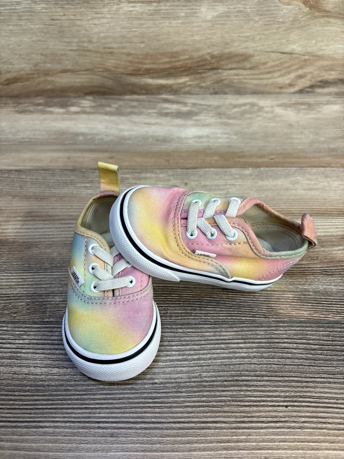 Three-quarter view of Vans toddler sneakers with pastel tie-dye canvas and elastic laces on wood background