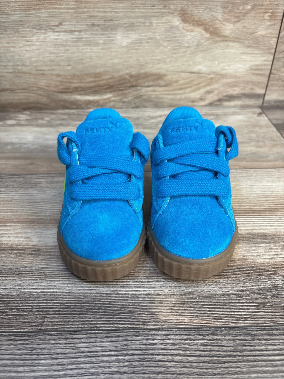 Front view of Puma Fenty blue suede toddler sneakers showcasing chunky laces embossed logo and gum platform soles on wood plank floor