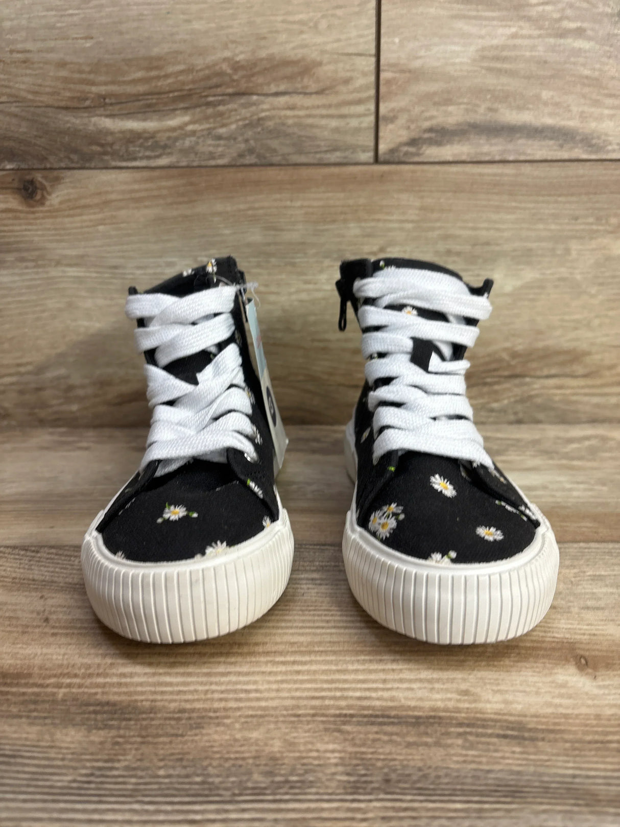 Black kids high-top sneakers with white daisy print and white laces on wood floor