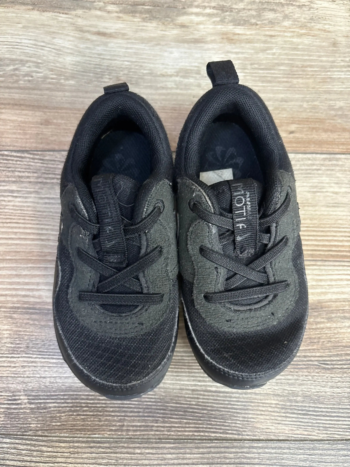 Top-down view of black Nike Air Max Motif PS sneakers showing mesh upper, elastic laces and heel pull tabs on wood floor