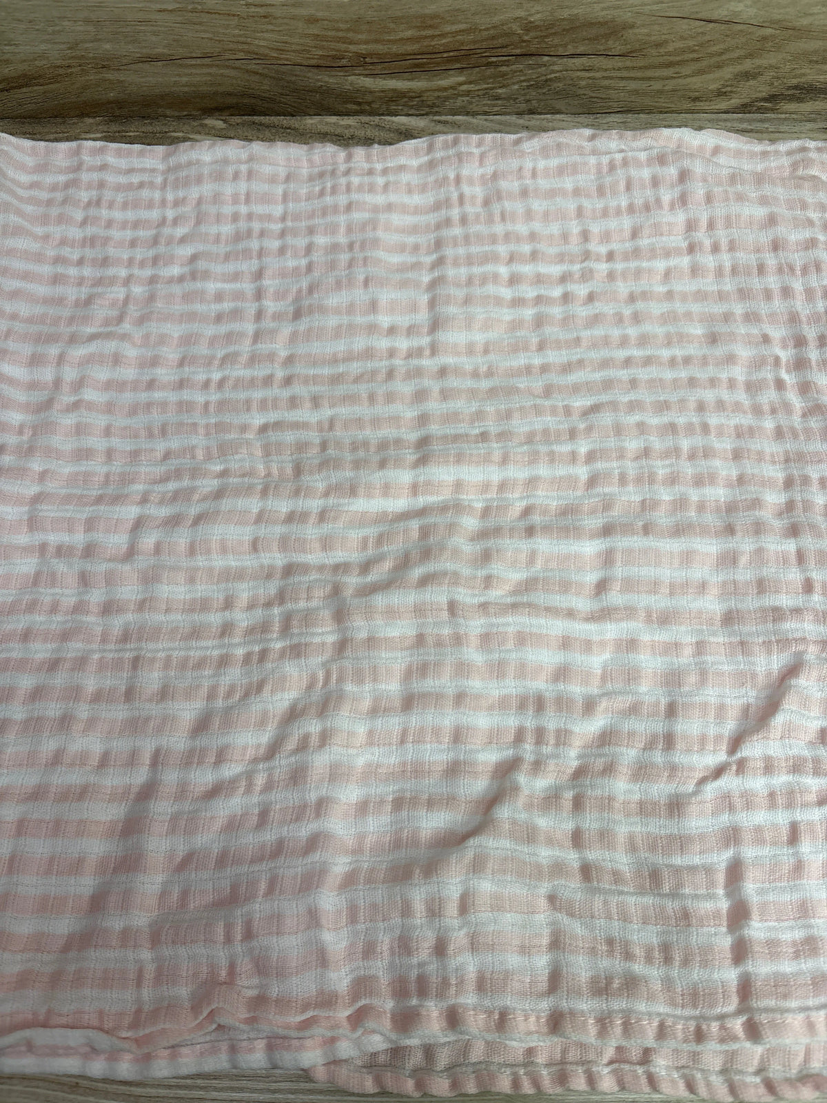 Top view of Chick Pea pink muslin swaddle blanket showcasing white stripes and textured fabric on a wood surface