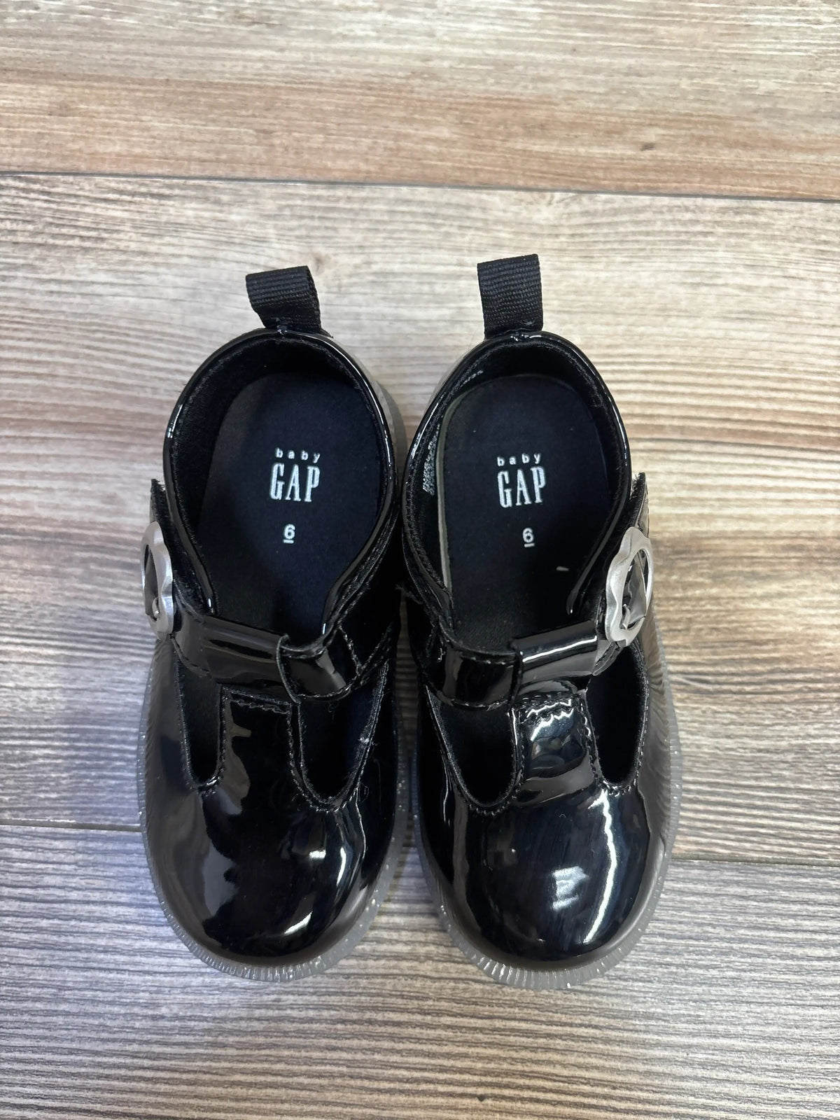 Top view of Baby Gap black T-strap loafers, size 6C, showing vegan patent leather and metal buckles on wood
